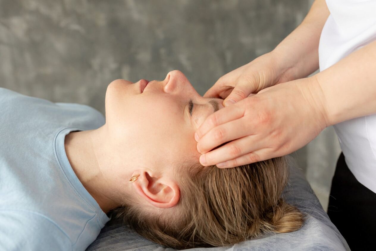 Practitioner's hands resting at the forehead and temple of a woman lying on a treatment table