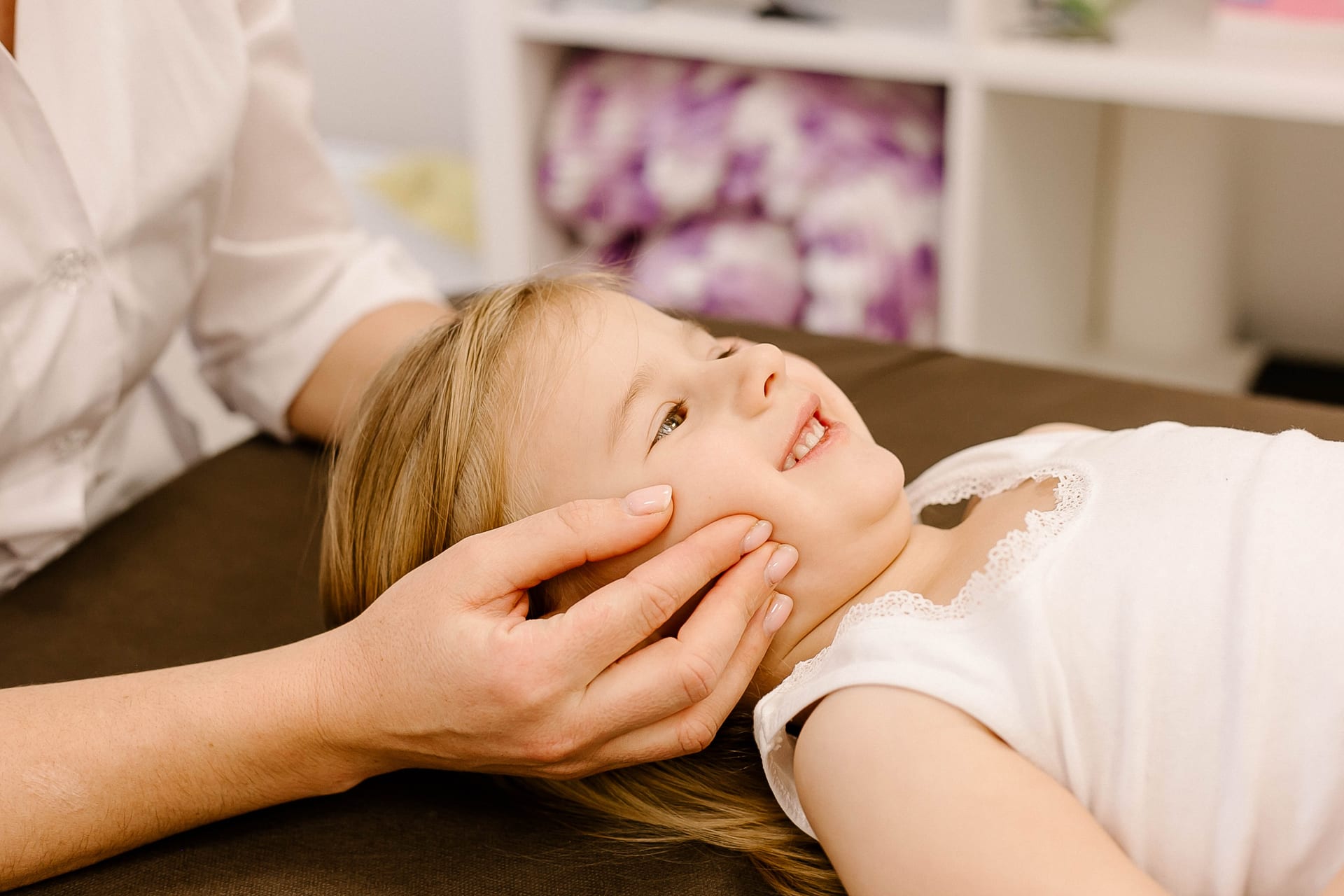 Smiling young girl receiving gentle craniosacral therapy on her jaw and face
