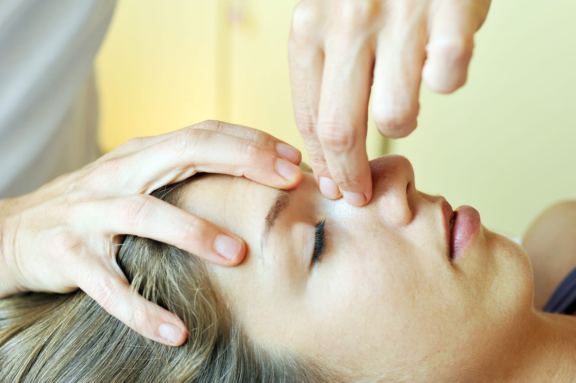 Practitioner placing both hands around a reclining client’s forehead and nose