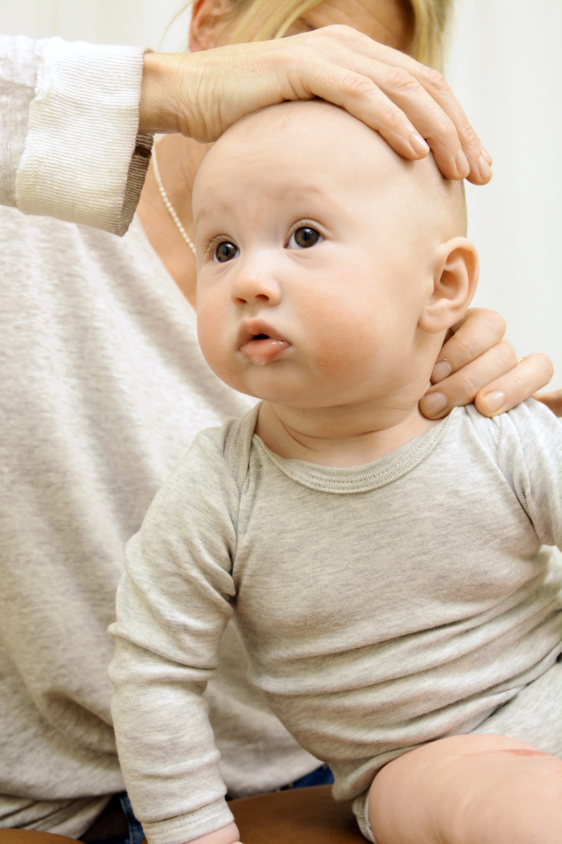 Clothed baby sitting up while a practitioner supports the crown of its head and shoulder